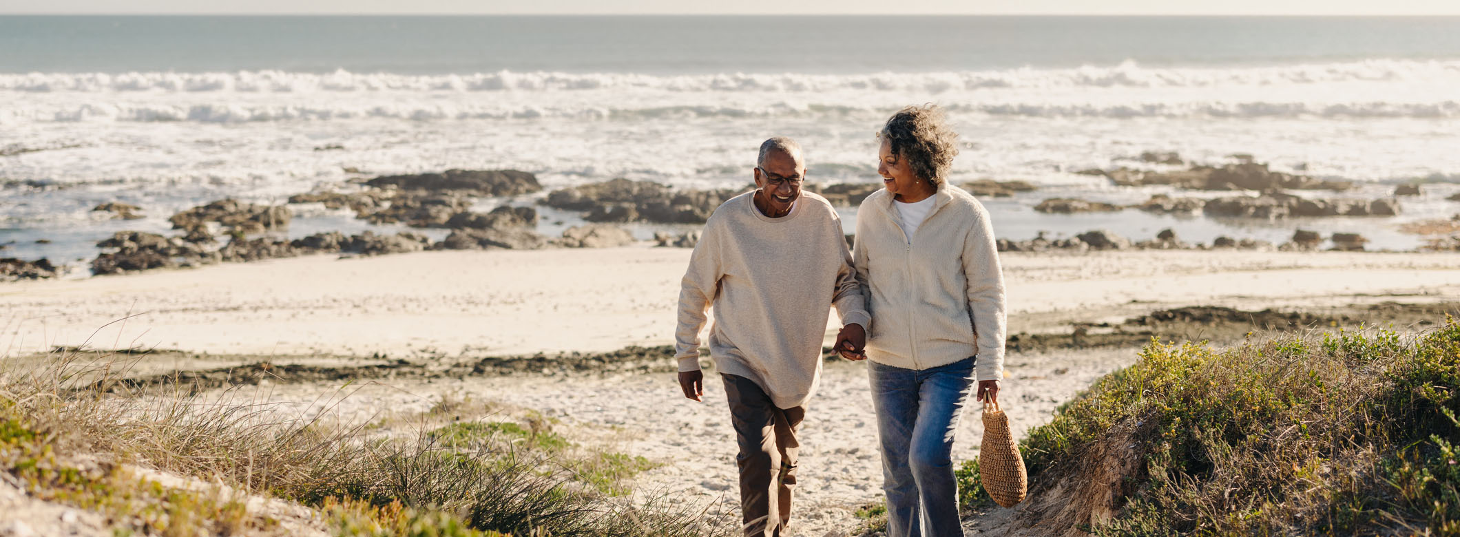 Older couple walking hand-in-hand along a beach path, representing the ease and reassurance supported by accurate tax preparation and long-term accountancy care.